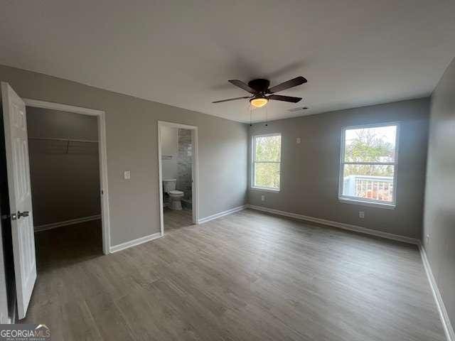 unfurnished bedroom with wood finished floors, baseboards, a closet, a walk in closet, and ensuite bath