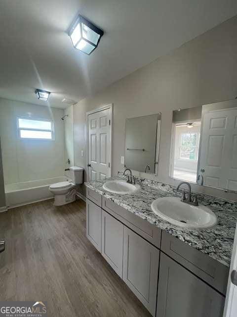 full bathroom with double vanity, a sink, toilet, and wood finished floors