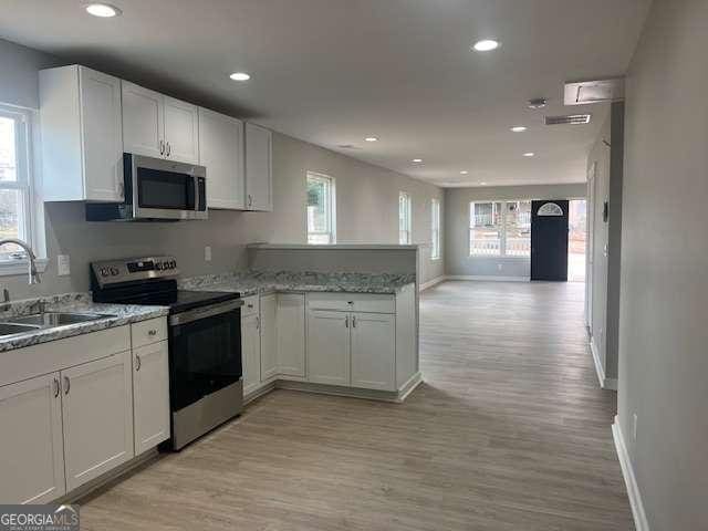 kitchen with white cabinets, appliances with stainless steel finishes, open floor plan, a peninsula, and a sink