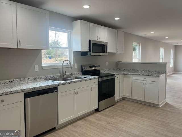 kitchen featuring stainless steel appliances, a peninsula, a sink, light wood-style floors, and white cabinets