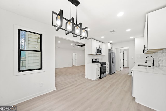 kitchen with decorative light fixtures, decorative backsplash, appliances with stainless steel finishes, white cabinets, and a sink