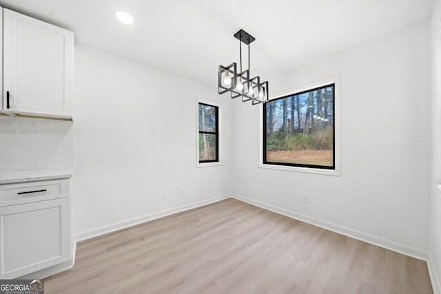 unfurnished dining area with a chandelier, recessed lighting, baseboards, and light wood finished floors