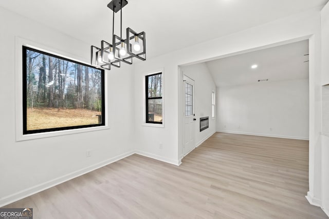 unfurnished dining area with a chandelier, vaulted ceiling, baseboards, and light wood-style floors