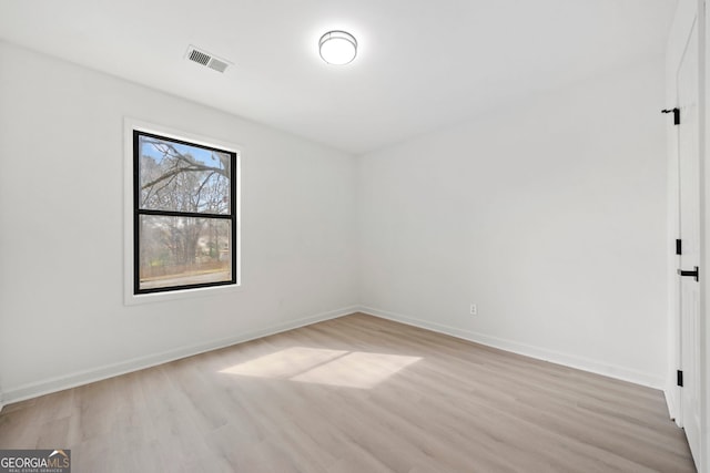 empty room with light wood-style floors, visible vents, and baseboards