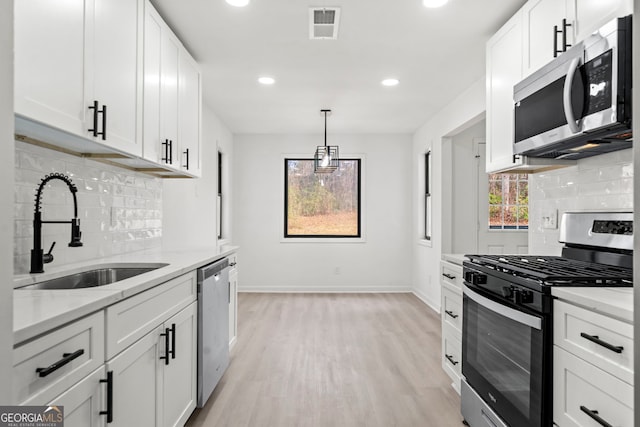 kitchen with stainless steel appliances, visible vents, white cabinets, a sink, and light wood-type flooring