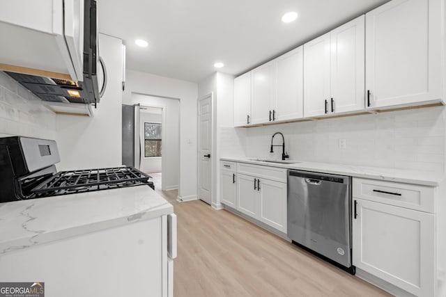 kitchen featuring stainless steel appliances, white cabinets, a sink, and light stone counters