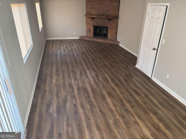 unfurnished living room featuring a brick fireplace, dark wood finished floors, and baseboards