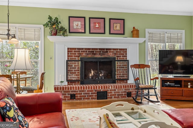 living room with a brick fireplace, crown molding, and wood finished floors