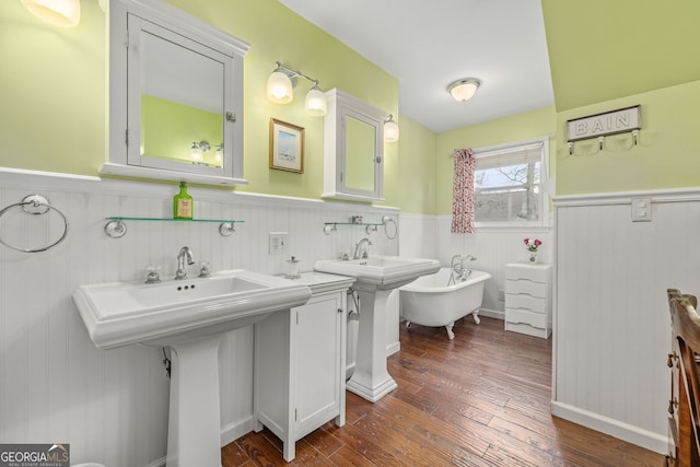 bathroom with a wainscoted wall, wood finished floors, two sinks, and a freestanding tub