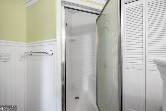 bathroom with a closet, a wainscoted wall, and a shower stall