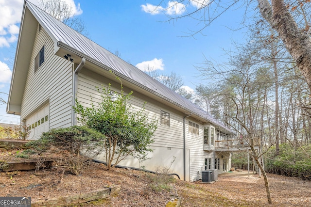 view of home's exterior with a standing seam roof, metal roof, a balcony, a garage, and cooling unit