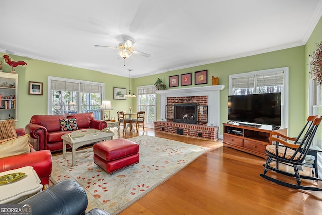 living area featuring a ceiling fan, a brick fireplace, crown molding, and wood finished floors