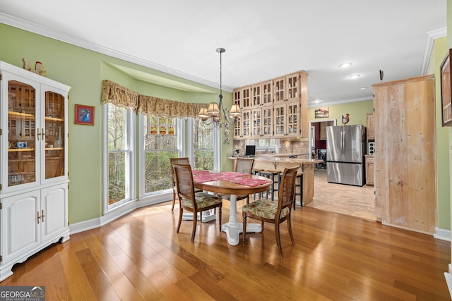 dining space with light wood-type flooring, baseboards, ornamental molding, and a chandelier