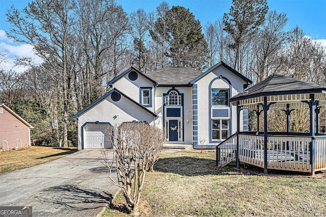 traditional home with a garage, driveway, a gazebo, a front lawn, and stucco siding