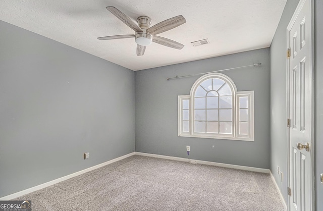 carpeted spare room featuring a ceiling fan, visible vents, a textured ceiling, and baseboards