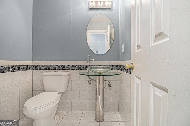 bathroom with wainscoting, a sink, toilet, and tile walls