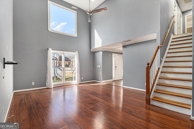 unfurnished living room with a towering ceiling, stairway, baseboards, and wood finished floors