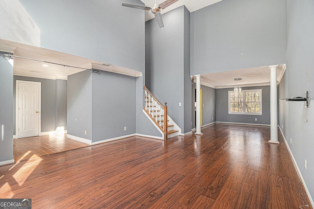 unfurnished living room featuring decorative columns, stairs, baseboards, and dark wood finished floors