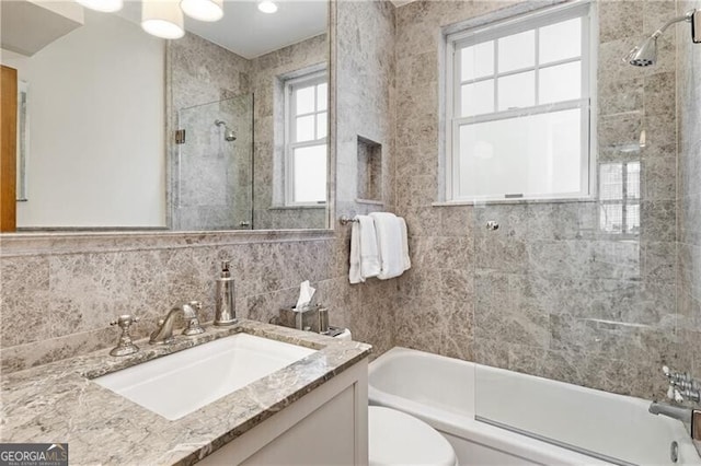 full bath with bath / shower combo with glass door, vanity, toilet, and tile walls