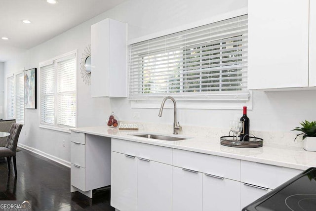 kitchen featuring recessed lighting, a sink, baseboards, white cabinets, and light stone countertops