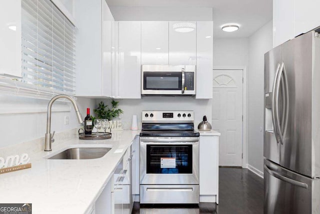 kitchen featuring stainless steel appliances, white cabinets, a sink, and light stone counters