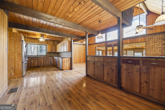 kitchen featuring brown cabinetry, dark countertops, decorative light fixtures, freestanding refrigerator, and beam ceiling