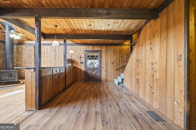 foyer with wood-type flooring, visible vents, a wood stove, beamed ceiling, and stairs