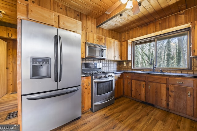 kitchen with dark countertops, wooden ceiling, appliances with stainless steel finishes, brown cabinets, and a sink