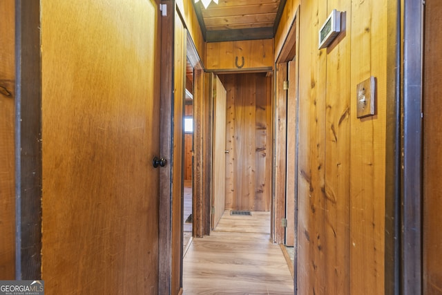 hall with light wood-style floors, wood ceiling, and wooden walls