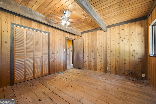 unfurnished bedroom with a closet, wood-type flooring, beam ceiling, and wooden walls