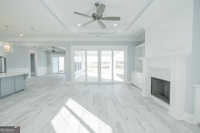 unfurnished living room featuring ornamental molding, a tray ceiling, a fireplace, and light wood-style flooring