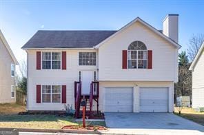 raised ranch with concrete driveway, an attached garage, and a chimney