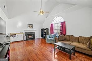 living area with wood finished floors, a lit fireplace, ceiling fan, and high vaulted ceiling