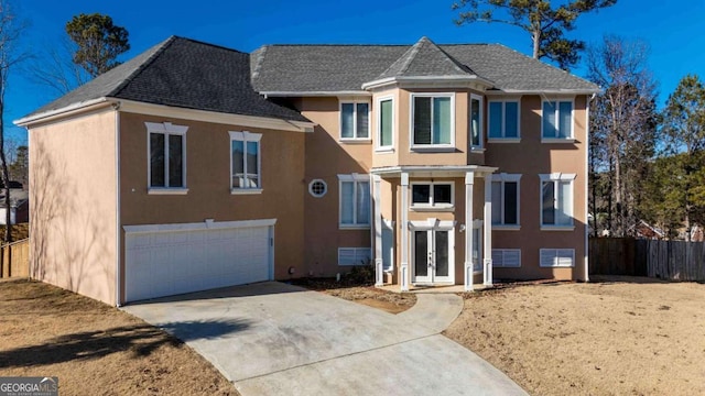 view of front facade with stucco siding, driveway, an attached garage, and fence