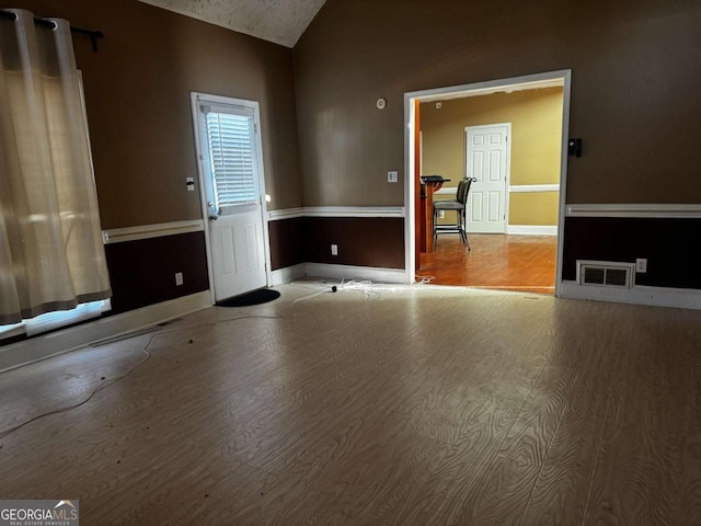 unfurnished living room with light wood-style floors, lofted ceiling, visible vents, and baseboards