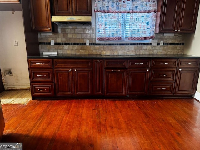 kitchen featuring dark wood-type flooring, backsplash, under cabinet range hood, and baseboards