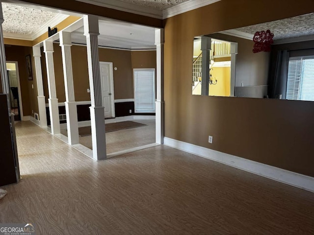 unfurnished room with decorative columns, ornamental molding, baseboards, and wood finished floors