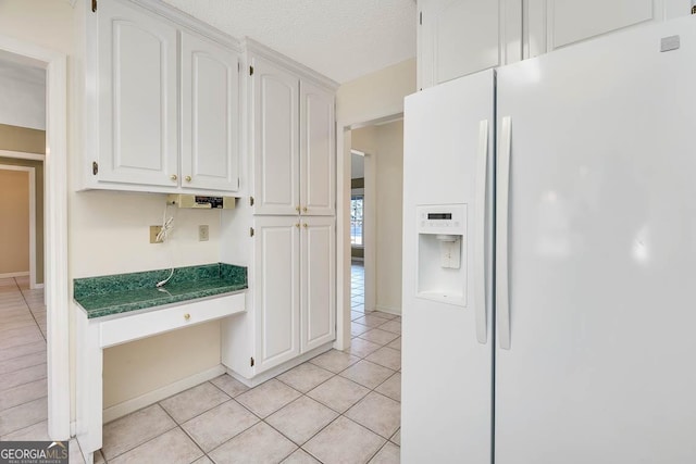 kitchen with white fridge with ice dispenser, built in desk, dark countertops, and white cabinets