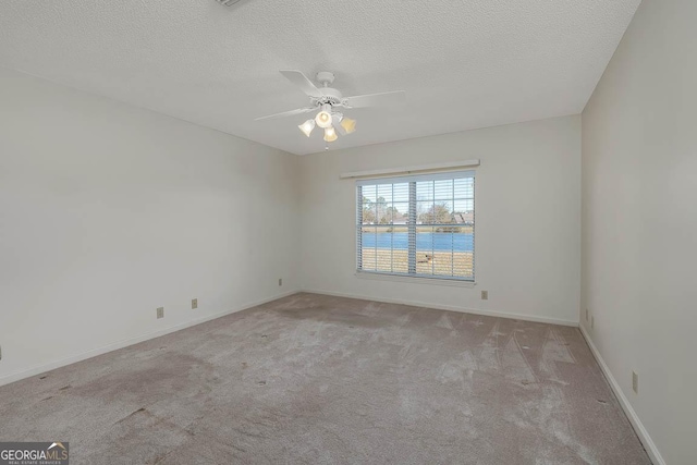 empty room featuring light carpet, baseboards, ceiling fan, a water view, and a textured ceiling