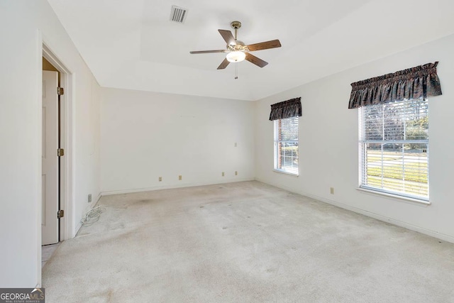 unfurnished room with ceiling fan, light colored carpet, visible vents, baseboards, and a tray ceiling