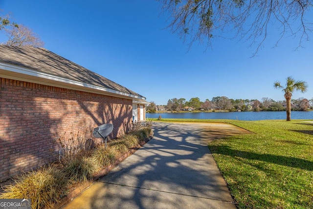 view of side of property featuring a water view, a lawn, brick siding, and roof with shingles