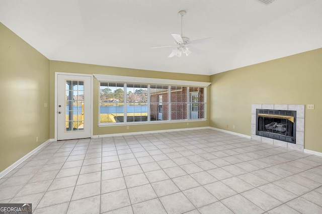 unfurnished living room featuring lofted ceiling, a water view, a tiled fireplace, ceiling fan, and baseboards