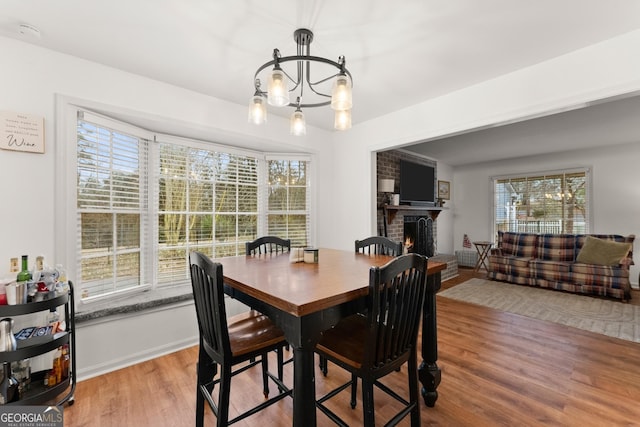 dining area with a brick fireplace, a healthy amount of sunlight, a notable chandelier, and wood finished floors