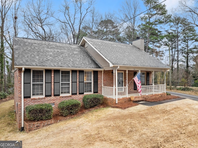 view of front facade with covered porch, brick siding, a chimney, and a shingled roof