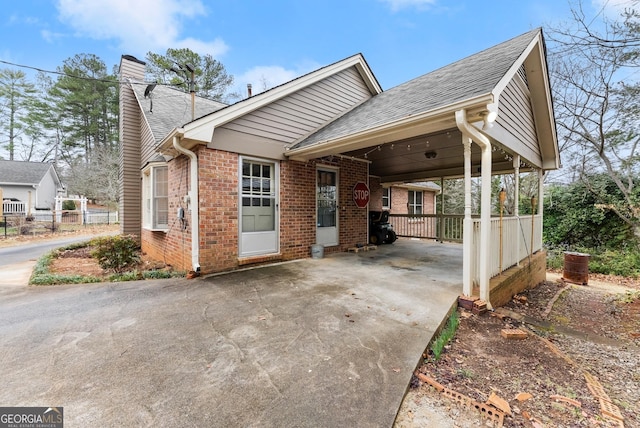 view of side of home with driveway, a chimney, roof with shingles, a carport, and brick siding