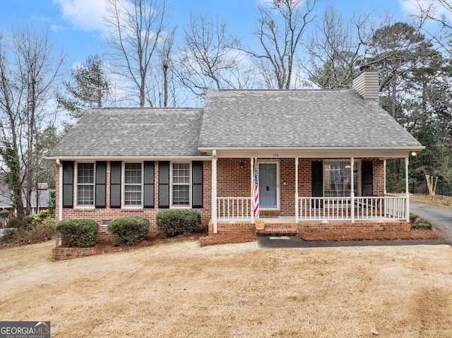 view of front of house featuring brick siding, roof with shingles, a chimney, a porch, and a front lawn