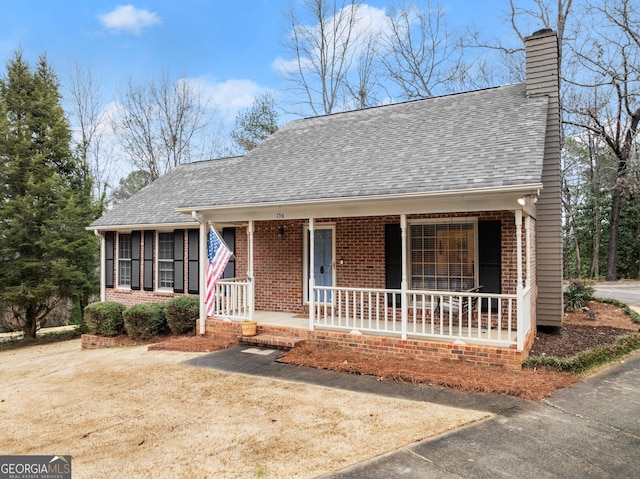 view of front of home with covered porch, brick siding, a chimney, and roof with shingles