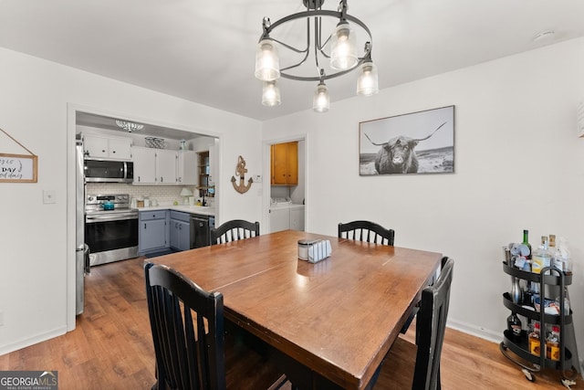 dining room with light wood-style floors, washing machine and dryer, a notable chandelier, and baseboards