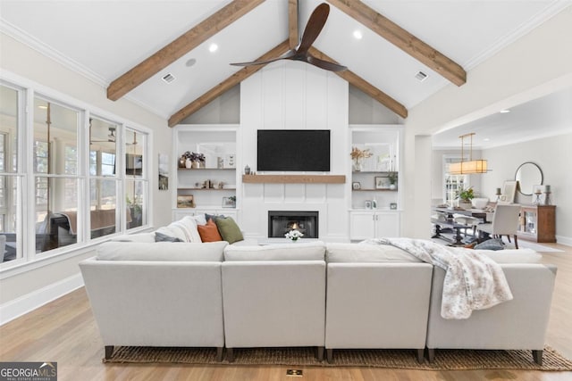 living room featuring light wood finished floors, a large fireplace, ceiling fan, beamed ceiling, and built in shelves