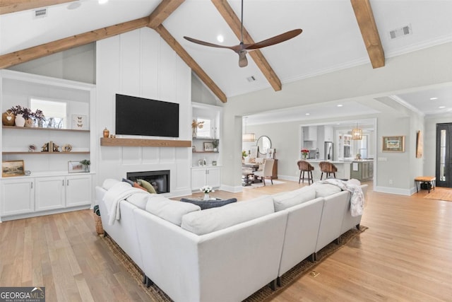 living area featuring built in shelves, a large fireplace, visible vents, light wood-style floors, and beamed ceiling